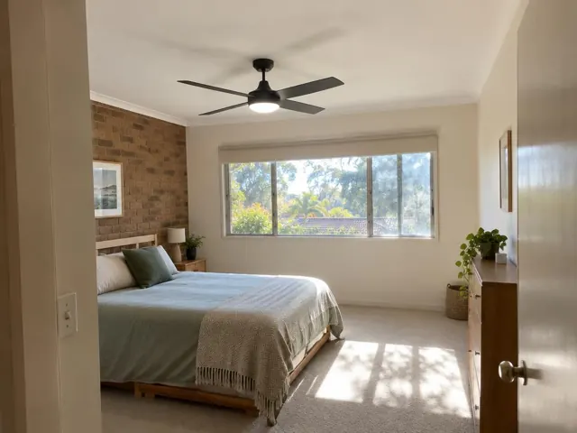 Ceiling fan in a bright bedroom with bed, window and brick feature wall in Meadowbank