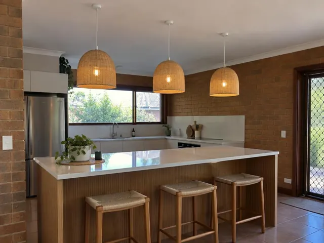 Kitchen with three woven pendant lights above a breakfast island, brick walls and tiled floor in Meadowbank