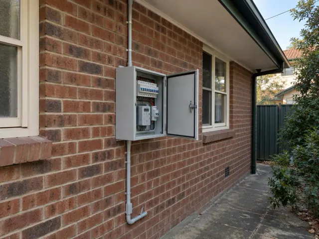 Exterior brick wall with an open electrical switchboard beside windows and guttering in West Ryde